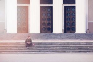 man sitting on steps with 3 doors behind